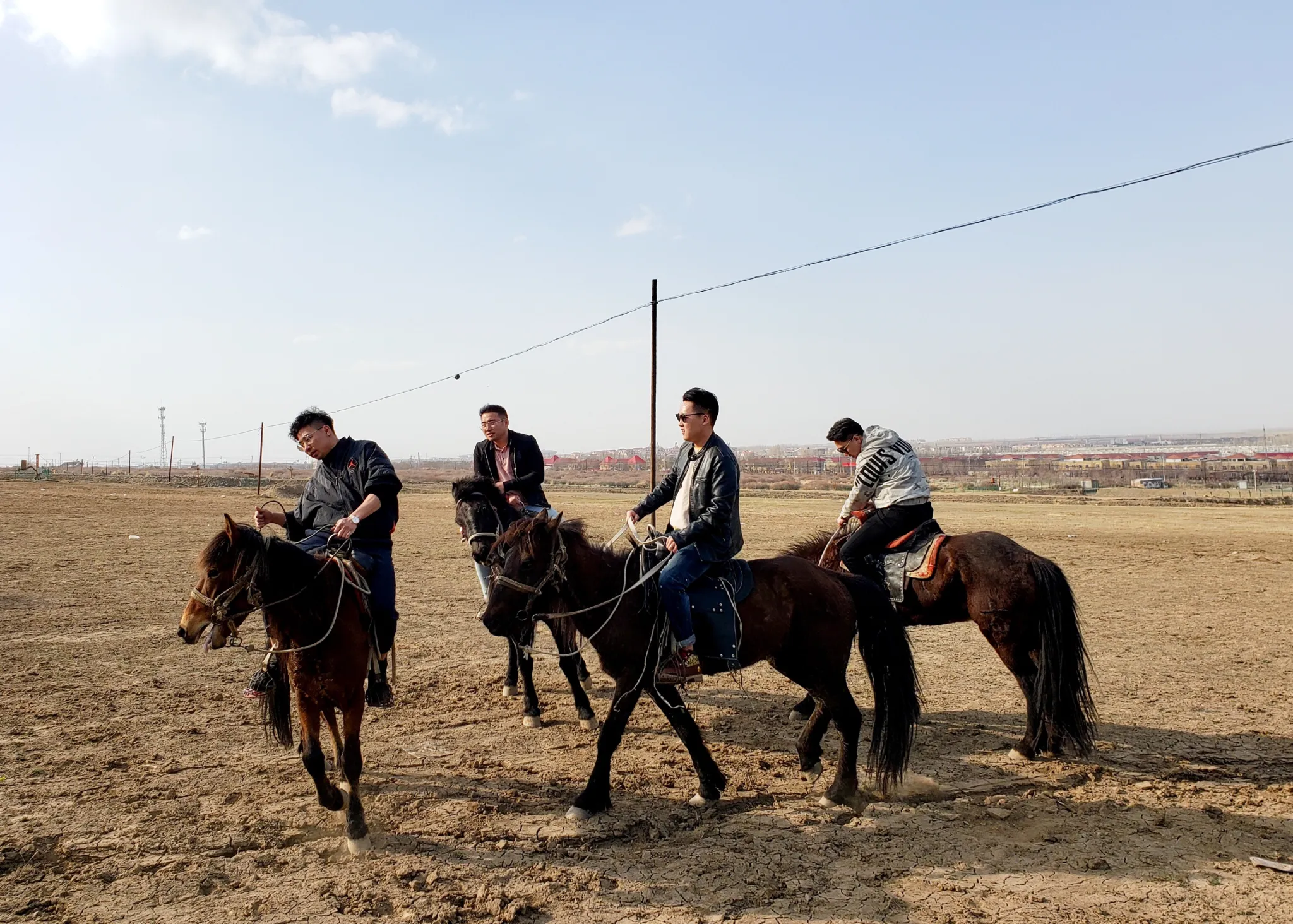 Four riders moving across a dry open landscape