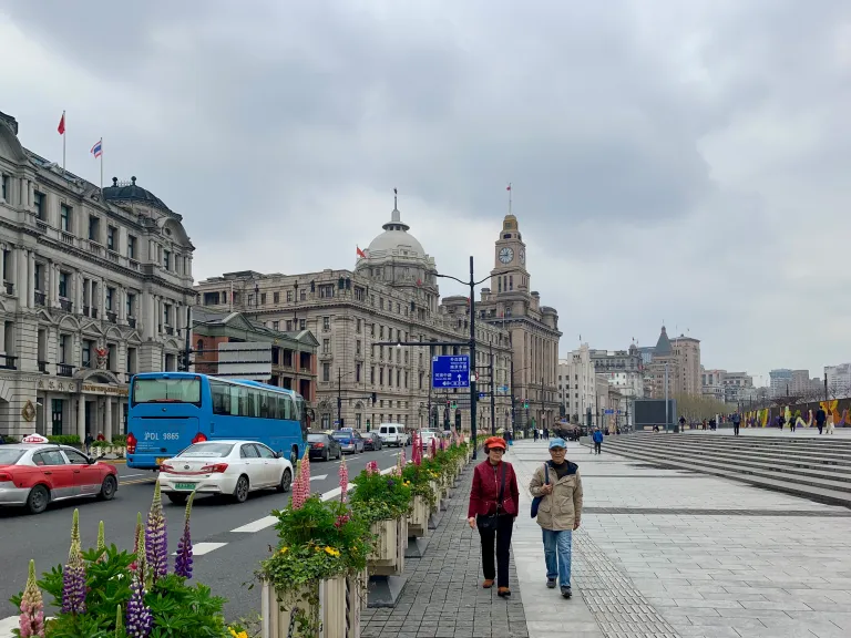 Two pedestrians walking beside traffic and flower planters on the Bund
