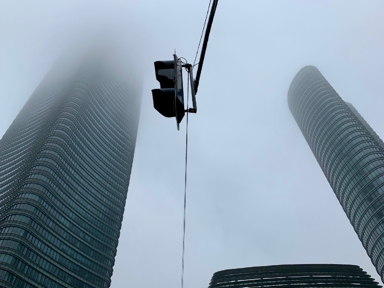 Two curved Shanghai towers framing a suspended traffic signal in fog