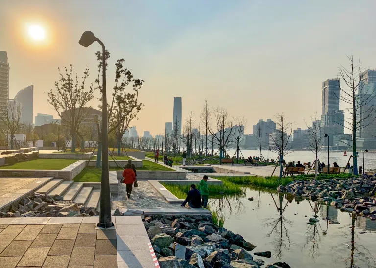 People occupying a landscaped waterfront park in Shanghai at sunset