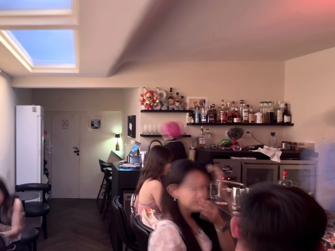 Guests seated at the long bar counter under warm pink light